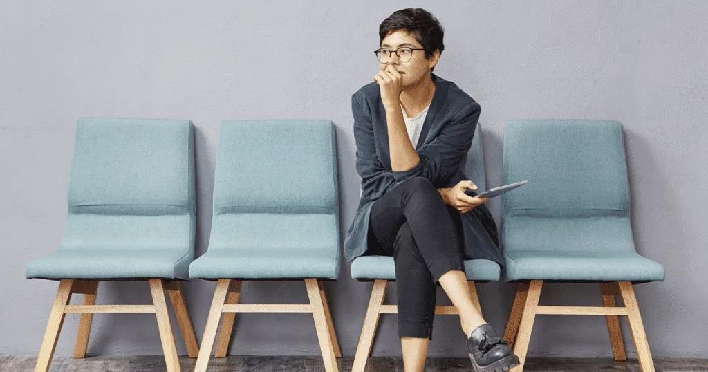 An employee sits in one of four blue chairs, deep in thought about work.