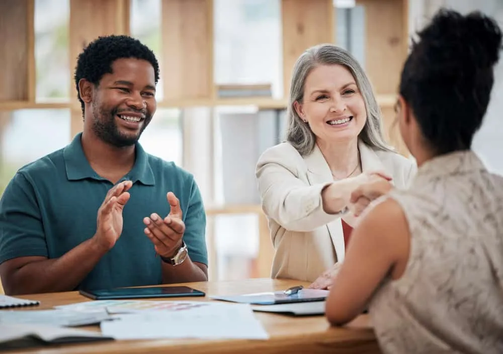 Smiling professionals shaking hands with a candidate after a successful job interview.