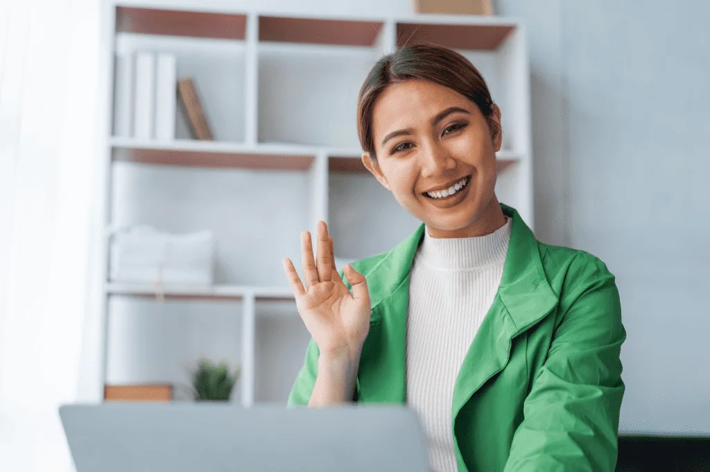 a-woman-waving-at-the-camera-on-their-laptop