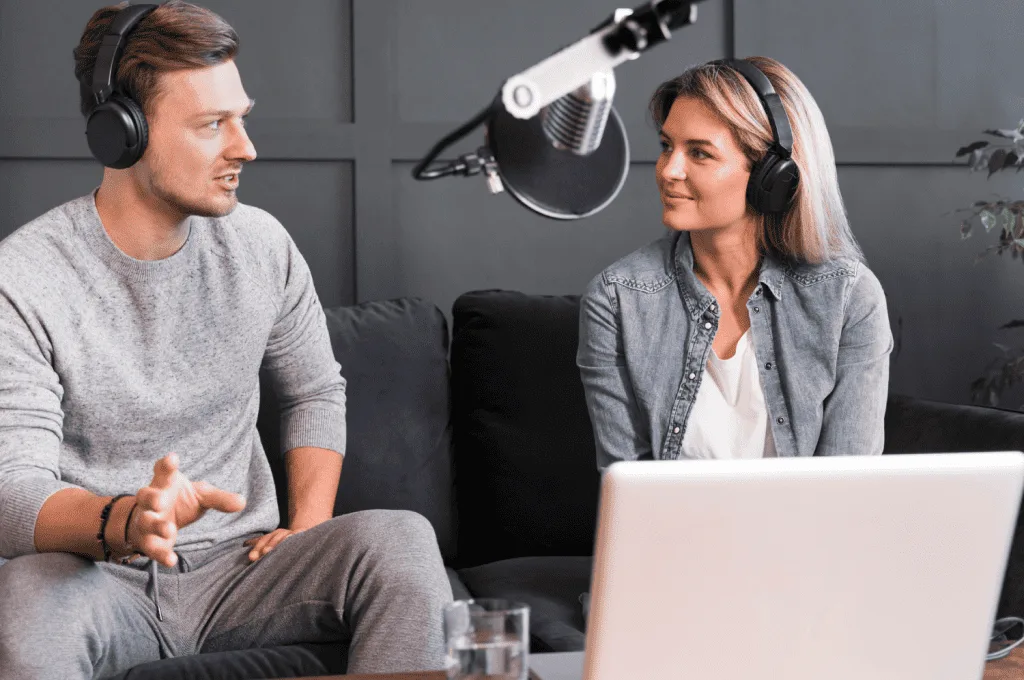 A man and a woman are engaged in a conversation about HR topics on a podcast, both speaking into microphones and wearing headphones.