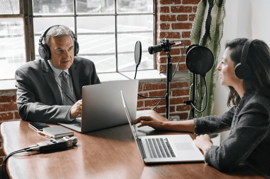 A female podcast host is asking a question about HR to a male guest, both wearing headphones and speaking into microphones.