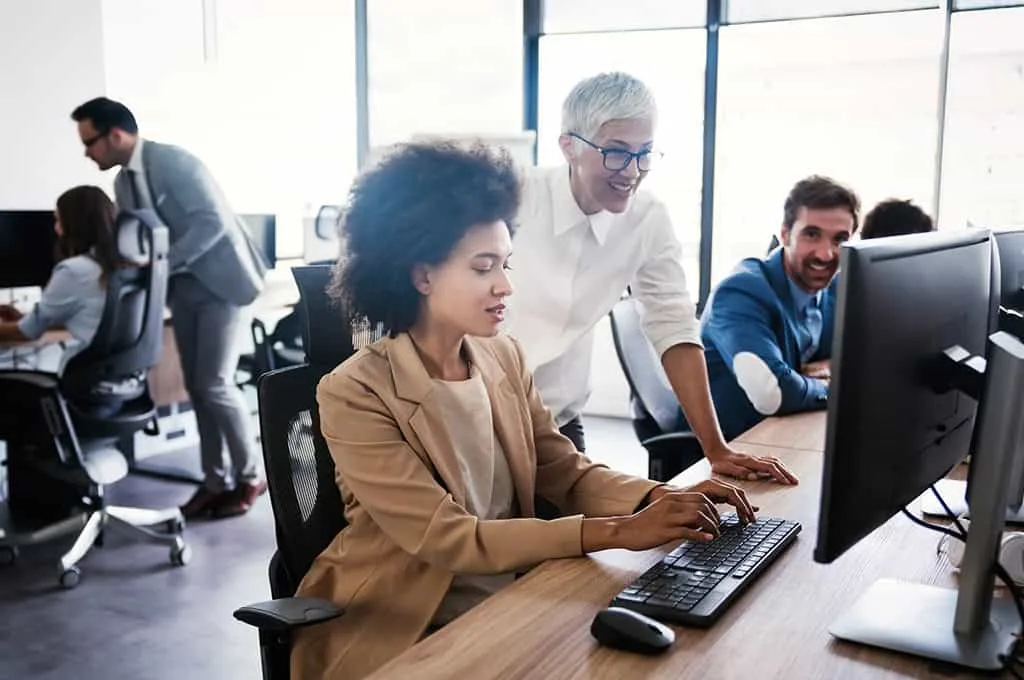 A team of three people, two women and a man, working together in an office, with other employees blurred in the background, depicting collaboration in utilizing email automation for HR tasks.