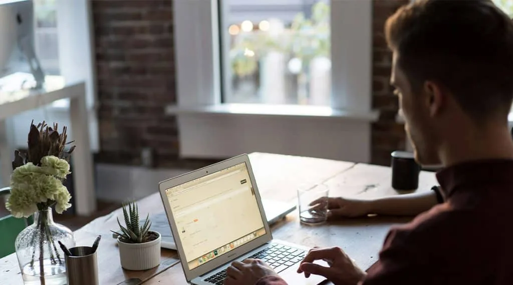 A man sitting at a desk in an office, focused on his laptop, illustrating the use of email automation in HR for efficient recruitment processes.